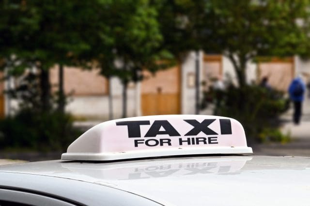 Close up view of a 'taxi for hire' sign on the roof of a taxi isolated against a blurred background.