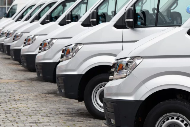 A line of identical white delivery vans neatly parked side by side