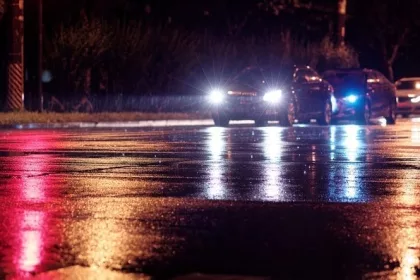 Rainy night in city, cars waiting on wet road because of red traffic light, rain was illuminated by the headlights of cars, focused on the asphalt road.