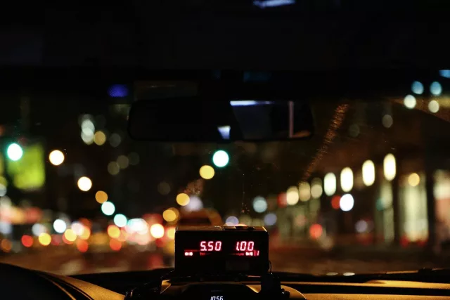 taxi meter on dashboard at night with city lights visible from the window