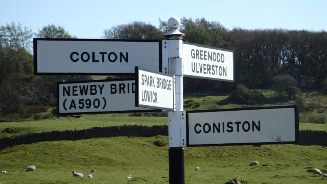 Destination sign post in the Lake District pointing to Colton, Greenwood Ulverston, Newby Bridge, Spark Bridge Lowick, and Coniston.