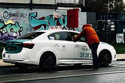 man in orange jacket leaning into the window of a white private hire taxi