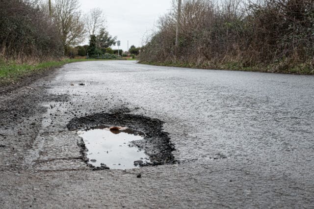 Deep road pothole filled with rainwater on British rural road