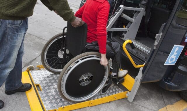 woman in wheelchair using ramp to get into a wheelchair accessible black taxi