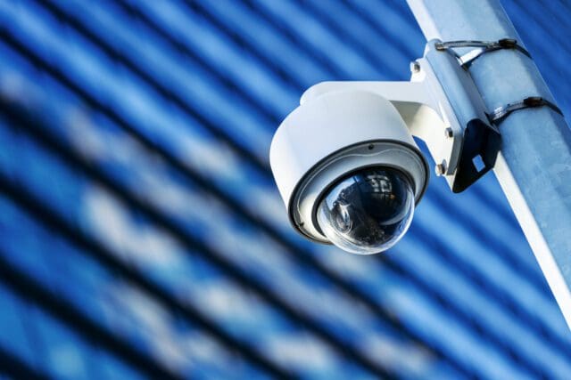 low angle shot of a white CCTV camera fixed onto a street pole with a skyscraper building in the background