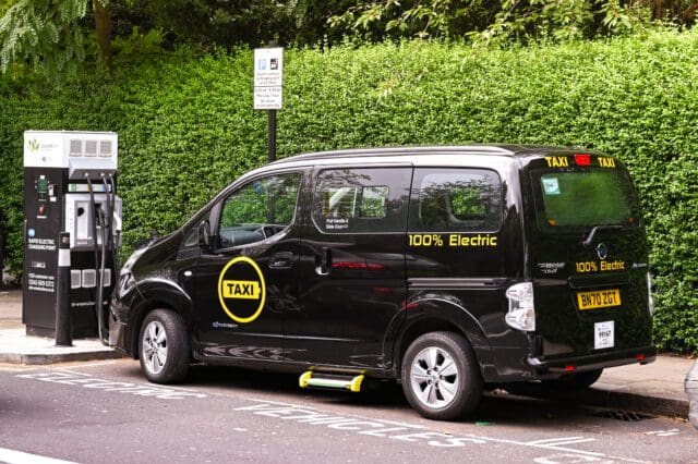 London taxi fully powered by electric connected to an electric charging station on a city street.