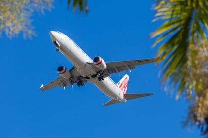 Virgin Atlantic airplane flying overhead on a clear blue sky day, framed by tropical palm trees.