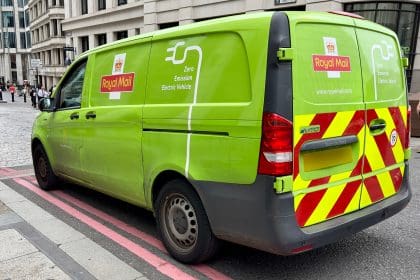 A green zero emission electric vehicle with Royal Mail branding parked in a city street in London, UK.
