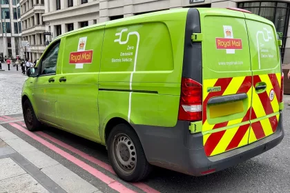 A green zero emission electric vehicle with Royal Mail branding parked in a city street in London, UK.