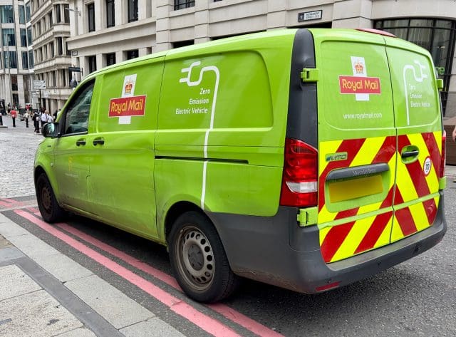 A green zero emission electric vehicle with Royal Mail branding parked in a city street in London, UK.