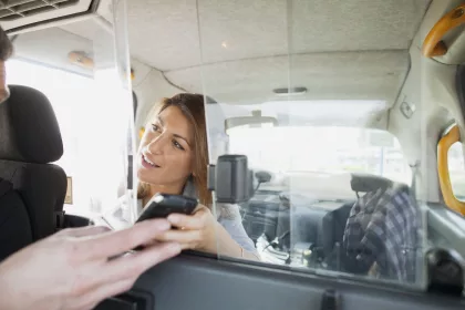 A Taxi Driver interacting with their customer. Looking at a mobile device, likely the one used to make the booking