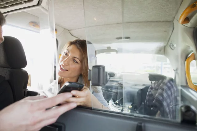A Taxi Driver interacting with their customer. Looking at a mobile device, likely the one used to make the booking