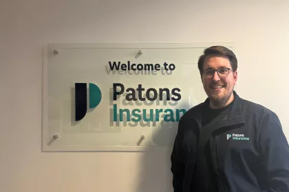 Patons Insurance marketing manager, Ben, pictured smiling next to Patons Insurance logo signage