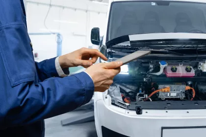 Serviceman with digital tablet next to electric van with open hood. EV maintenance.