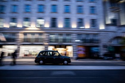 Taxi driver operating black taxi in London City at evening with passengers in it. Panning effect.