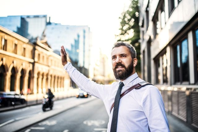 Businessman standing on the street in England, raising his hand to hail a taxi cab.