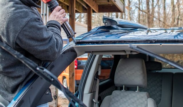 worker uses tools to remove a broken window in a car and replace with new glass