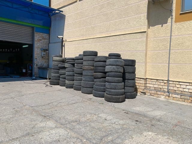 Stack of used car tires near the wall of a building on asphalt in a sunny day. Urban scene next to an auto repair shop.