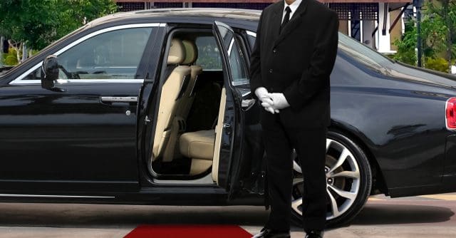 chauffeur driver standing next to opened car door with red carpet