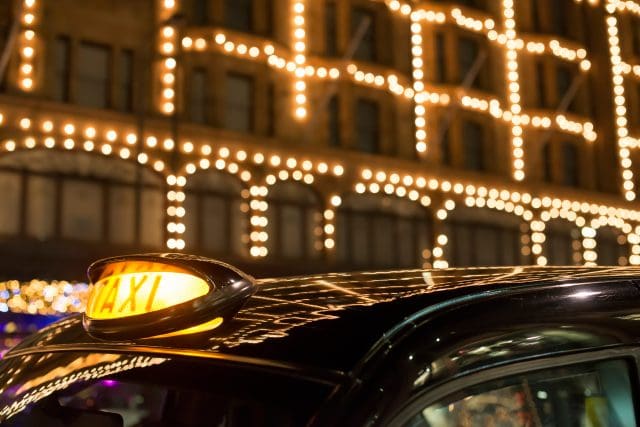 Black cab taxi in front of a shopping center with Christmas lights at night time