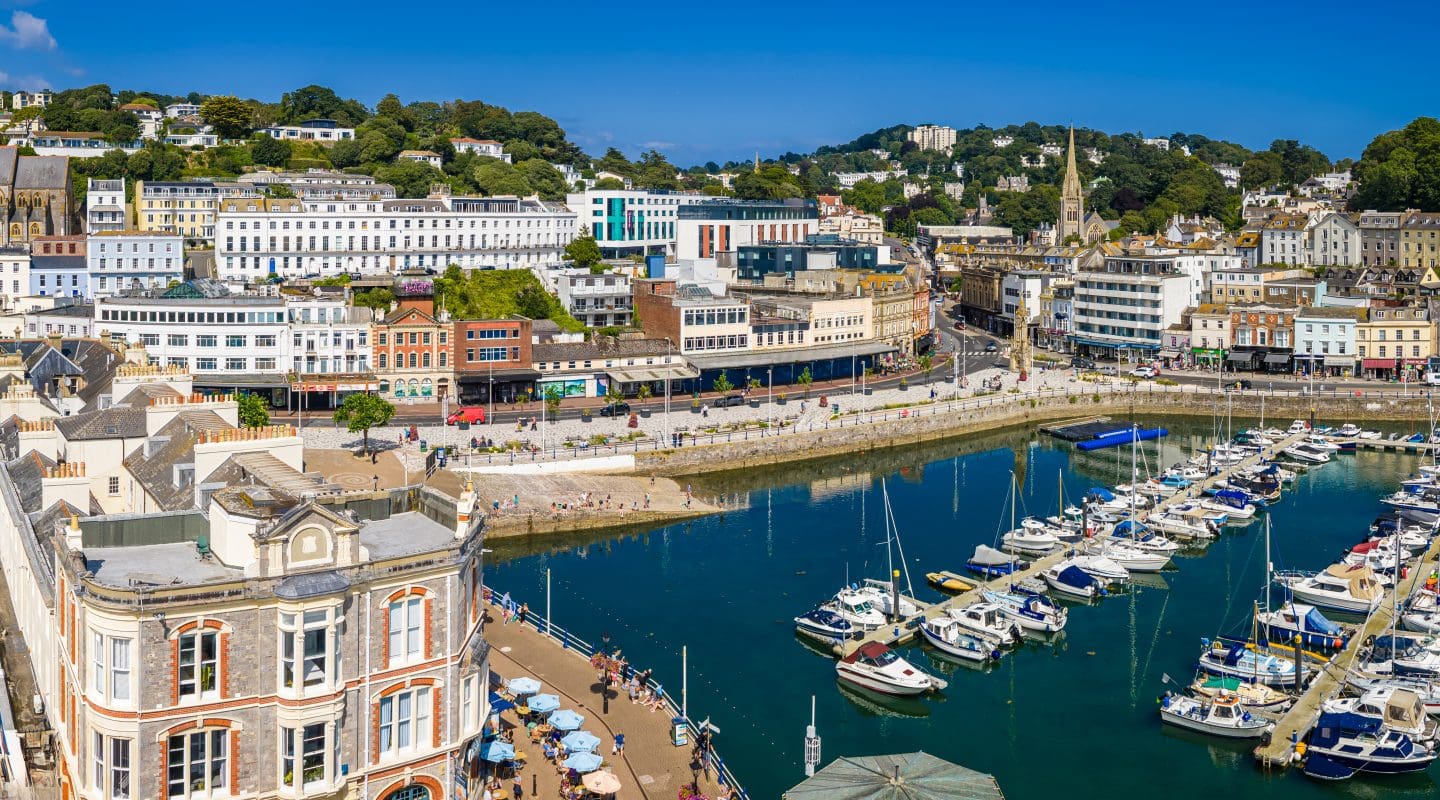 Drone view over Torquay Marina with sailboats, yachts, clear skies and turquoise waters.