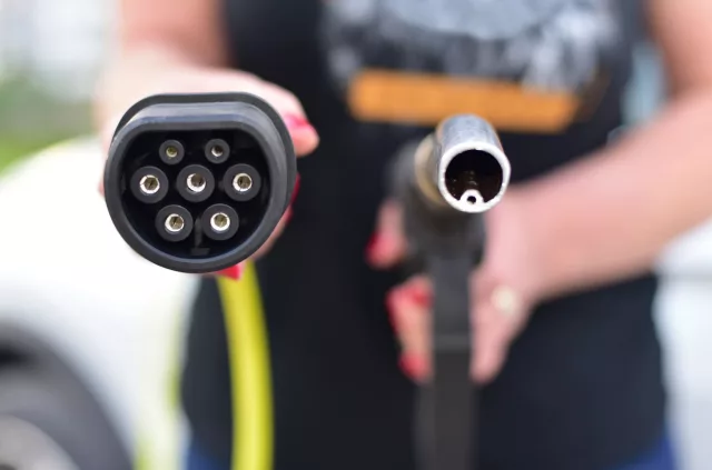 Fuel nozzle and electric car charger plug in hands. Electric cars or petrol and diesel cars.