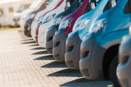 Fleet of vans in different colors sit neatly in a parking lot under a clear sky, highlighting their distinctive designs and shapes.