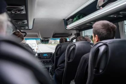 Interior view of a minibus with passengers seated as the vehicle travels along a road.