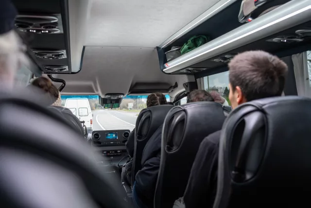 Interior view of a minibus with passengers seated as the vehicle travels along a road.