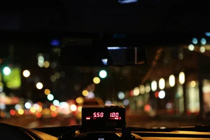View from inside a taxi at night, looking through the windshield onto a city street. A taxi meter is visible on the dashboard.