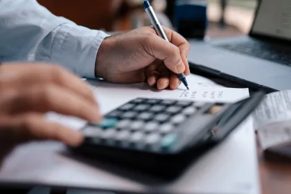 A person calculating finances with a calculator and pen on a desk.