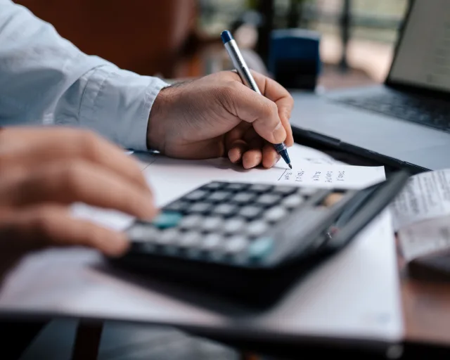 A person calculating finances with a calculator and pen on a desk.