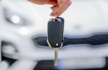 close up of hand holding a car key, with a white vehicle out of focus in the background