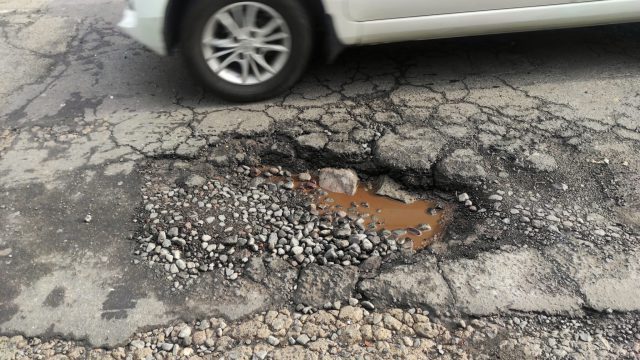 Wet hole and cracked on broken street in urban area