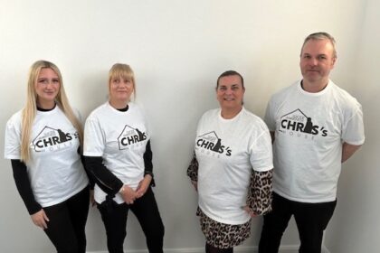 Patons insurance staff stood together in front of a white wall wearing t-shirts with the chris's house charity logo on front