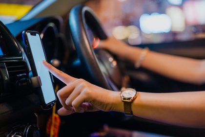 woman driver with one hand on the steering wheel and the other hand tapping smartphone screen